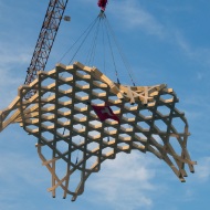 Photo d’une immense pièce de forme libre suspendue en hauteur sur la grue pour montage