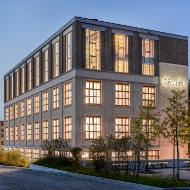 Aussenansicht des neu umgebauten Givaudan Bürogebäudes mit hell erleuchteten Fenstern.