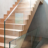 Un escalier sobre avec des marches en bois et une balustrade en verre relie le sous-sol au rez-de-chaussée.<br/><br/><br/><br/>