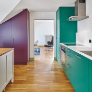 Fitted kitchen with cupboard doors in an accenting colour and wooden floor