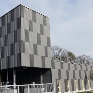 Architektonischer 250 m³ Modulsilo mit hell- und dunkelgrau karierter Fassade aus Holz optisch integriert in einen grösseren Gebäudekomplex.
