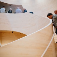 Besucher bestaunen die geschwungene Holztreppe im Atrium des Stammhauses von Blumer Lehmann beim 150-jaehrigen Jubilaeum.