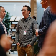 Gaeste im Gespraech mit Weinglaesern beim 150-jaehrigen Jubilaeum von Blumer Lehmann – lockere Networking-Atmosphaere.