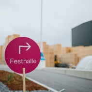 Pinkes Wegweiser-Schild mit Pfeil und der Aufschrift „Festhalle“ auf dem Firmengelaende von Blumer Lehmann beim 150-jaehrigen Jubilaeum.