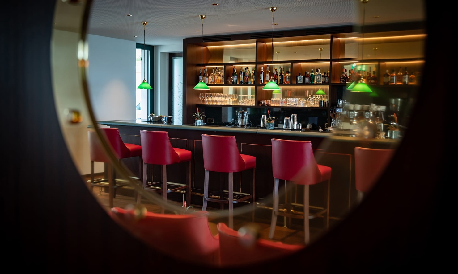 View of the bar at Hotel Bad Horn with red bar stools, seen through the porthole in the door