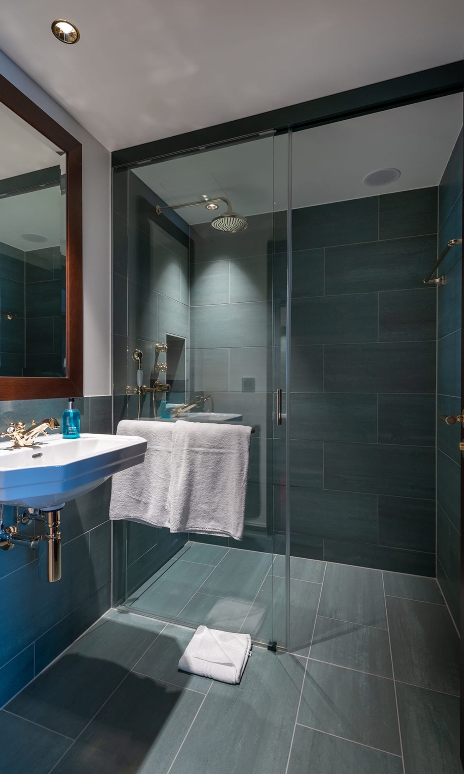 Dusche in einem Gästezimmer des Hotel Bad Horn mit grauen Fliesen und Glastüre und weisses Lavabo <br/><br/>