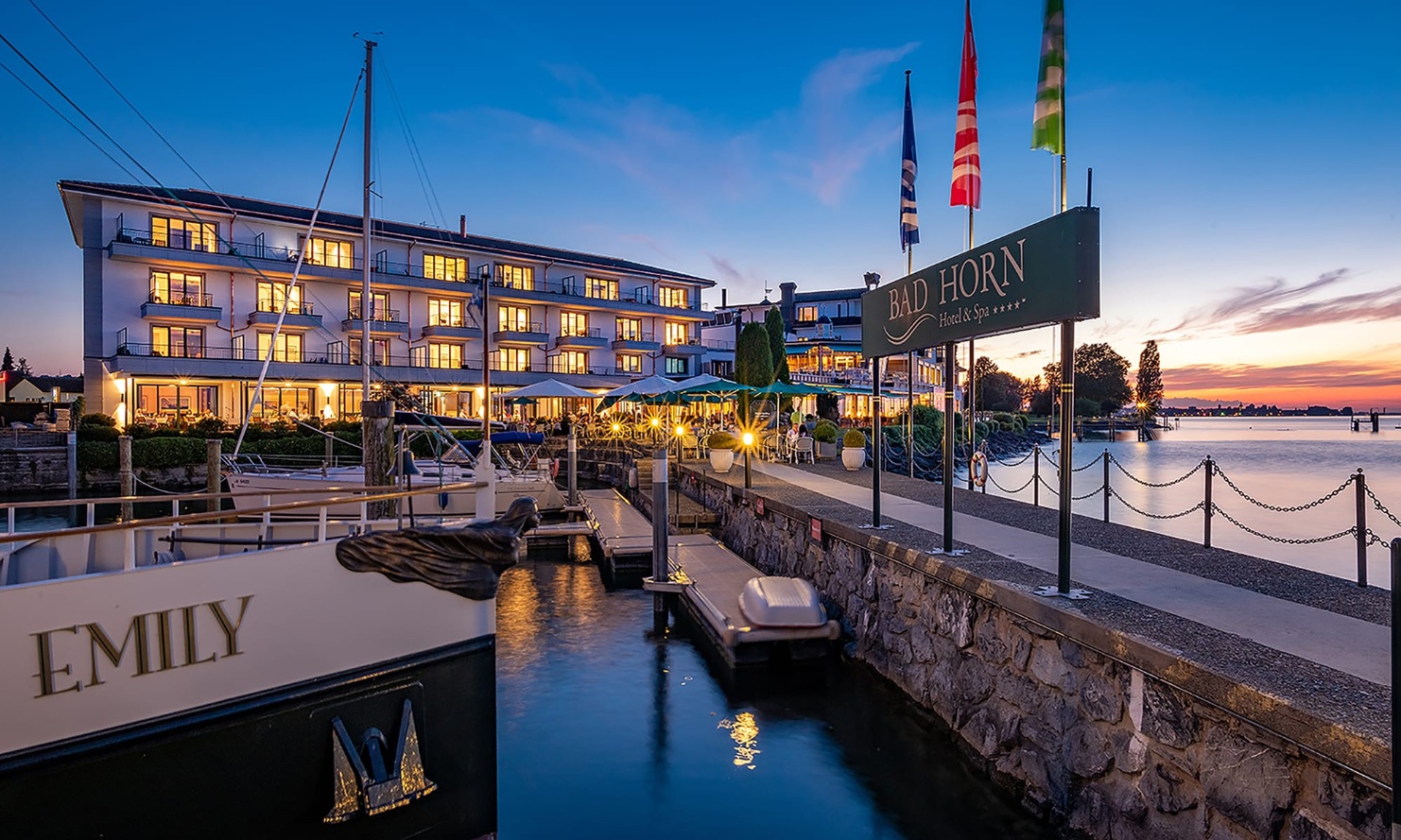 Hotel Bad Horn mit hell erleuchteten Fenstern und mit Schiffsteg sowie Booten davor