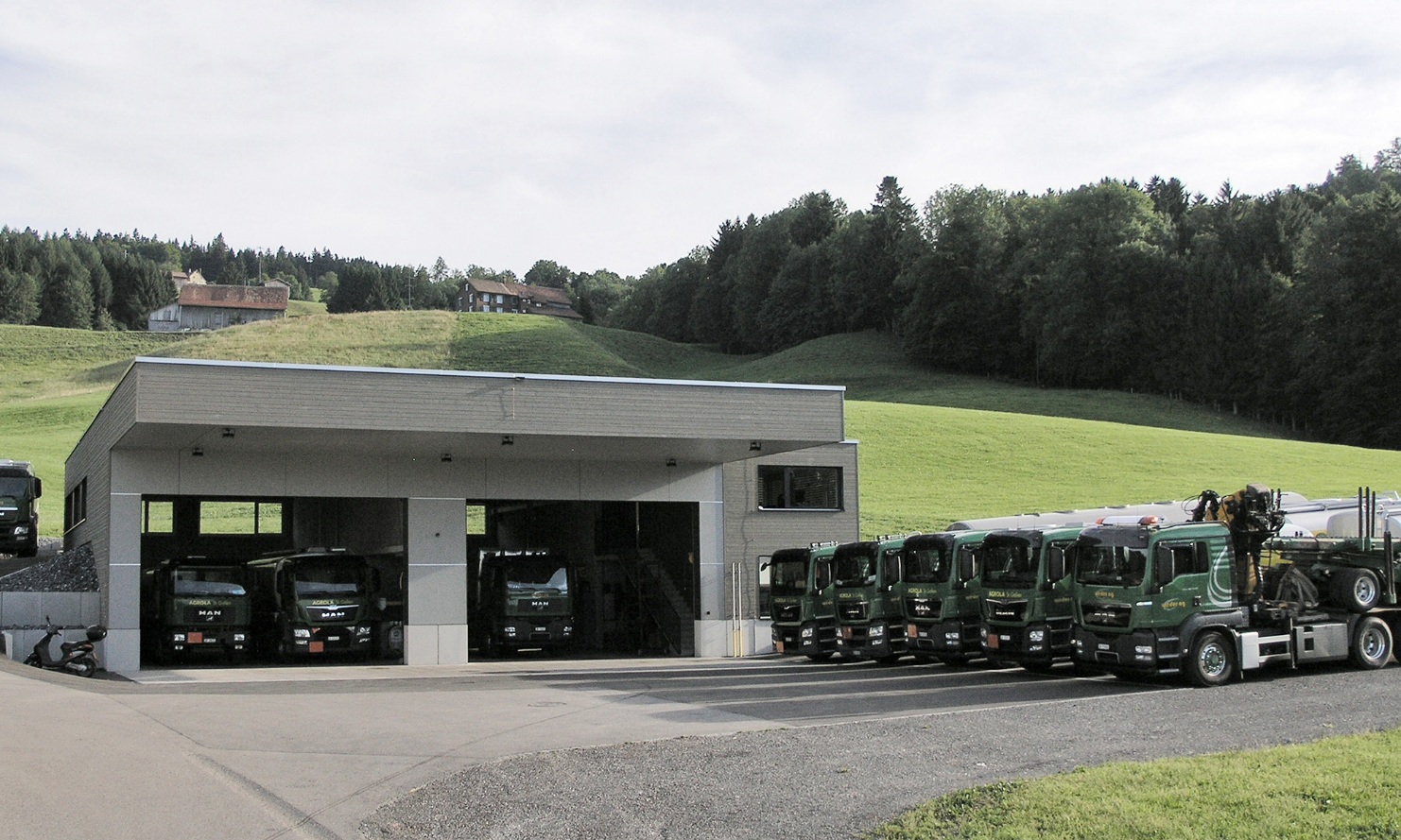 Gesamtansicht der Lkw-Einstellhalle mit parkierter Lkw-Flotte davor. 