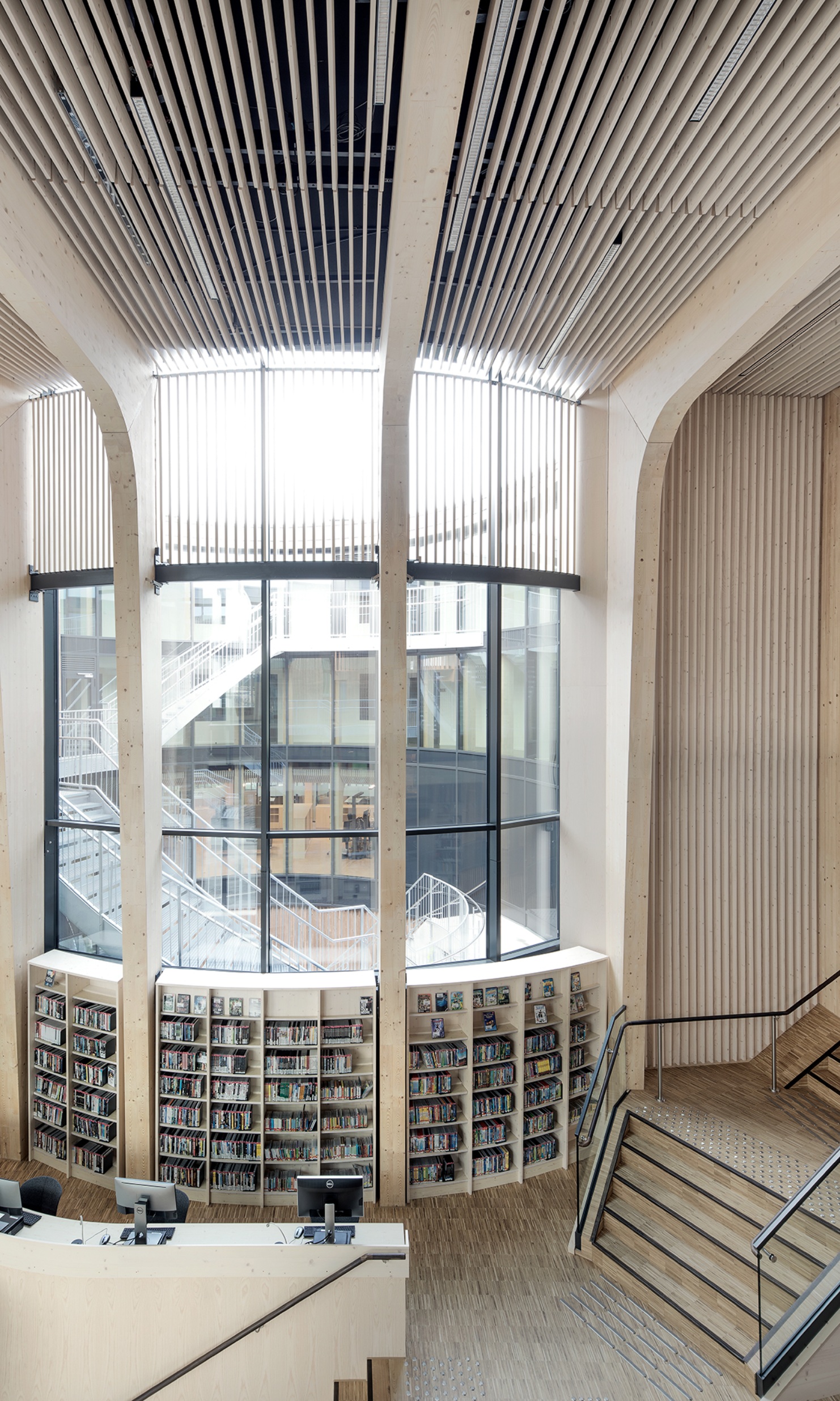 Helle Bibliothek mit Treppe, Bücherregalen und grosser Fensterfront.