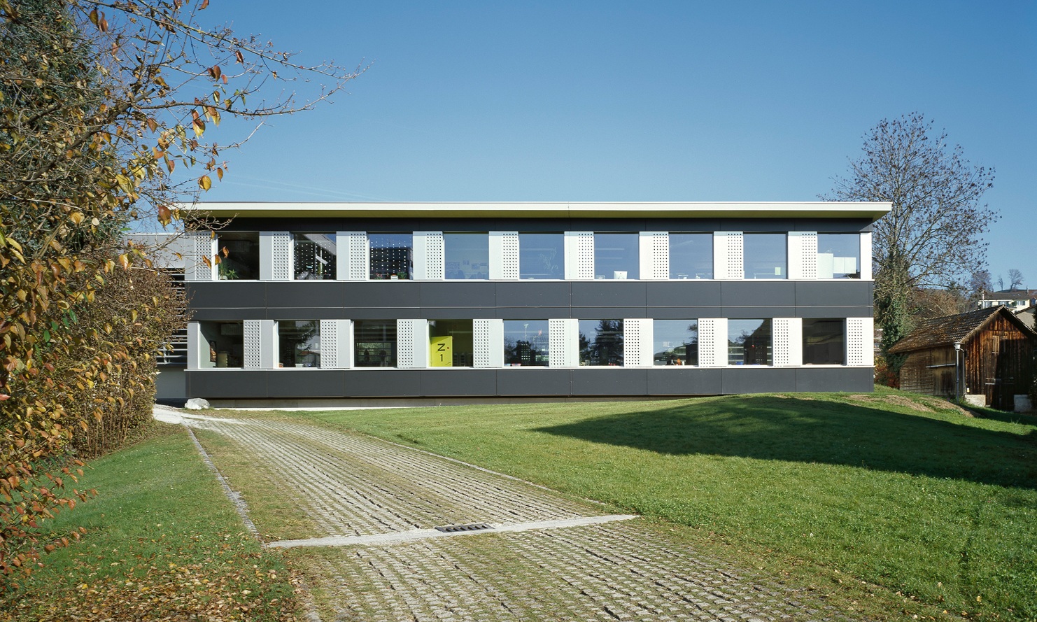 Zweigeschossiger temporärer Schulpavillon Hasenacker in Männedorf steht auf grüner Wiese.