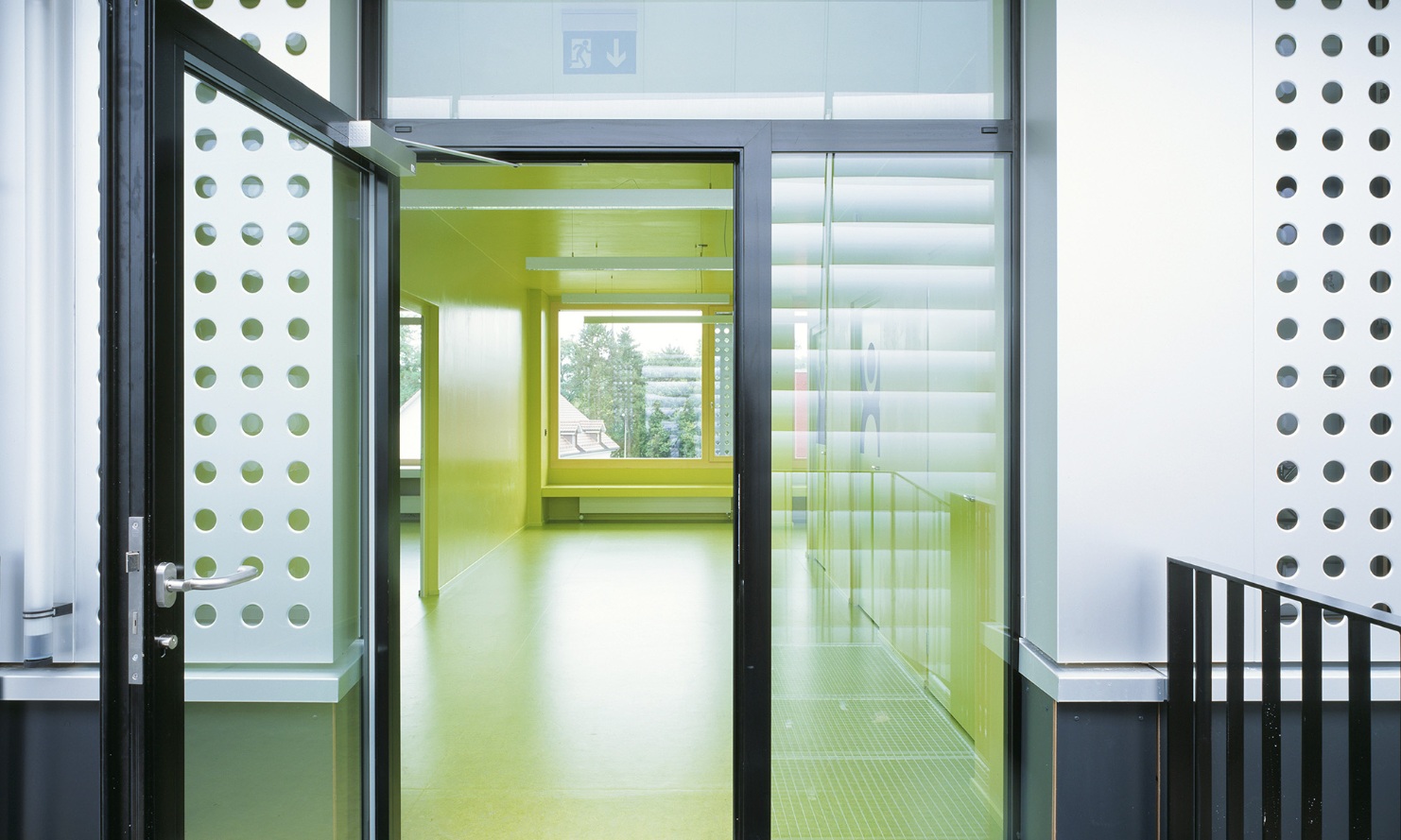 Einladen gestalteter Eingangsbereich des temporären Schulpavillons in Männedorf mit Glastüre und gelben Boden im Eingangsbereich.
