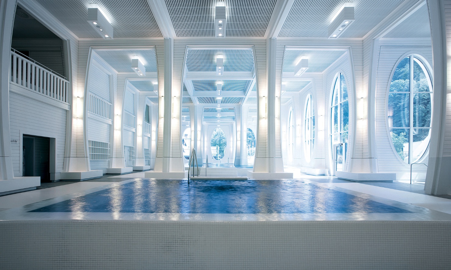 Piscine dans une pièce à colonnes blanches et plafond à habillage en bois.