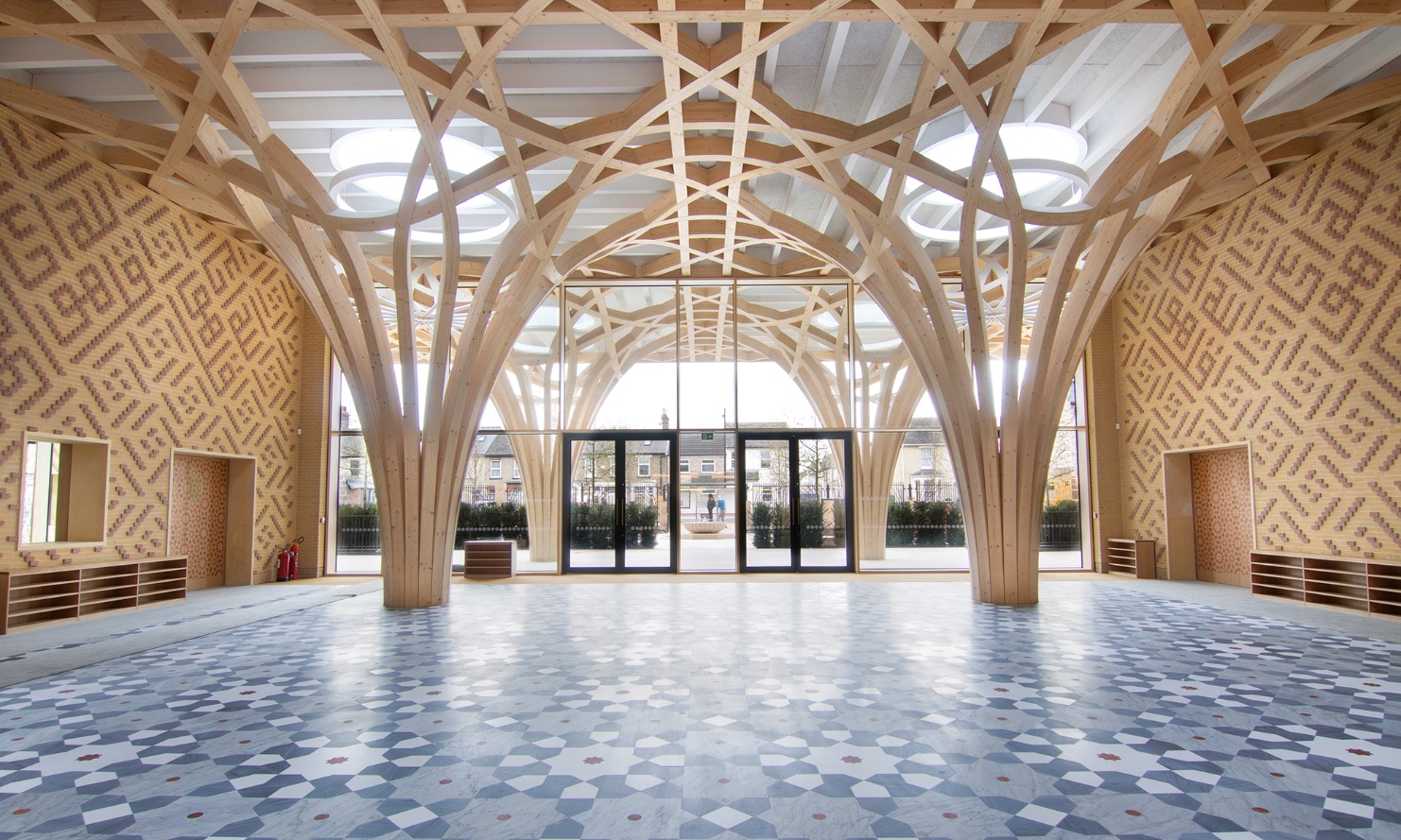 Die baumartige holzige Tragstruktur dominiert den Eingangsbereich der Cambridge Mosque. Der Fussboden ist mit einem grau-blauen Plattenmosaik gestaltet und die Wände mit zweifarbigen Klinkersteinen mit orientalischen Motiven. 