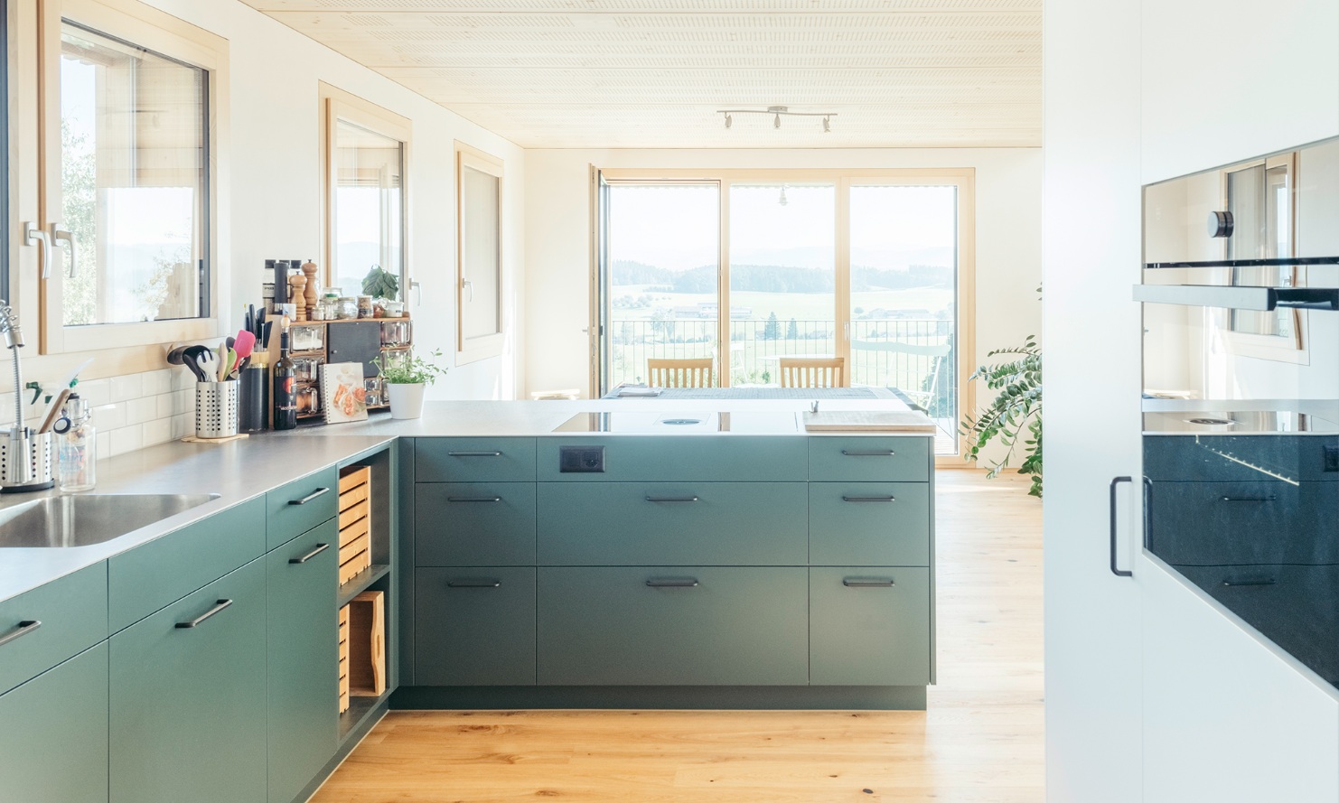 La cuisine moderne aux façades gris-vert est ouverte sur la salle à manger avec balcon.