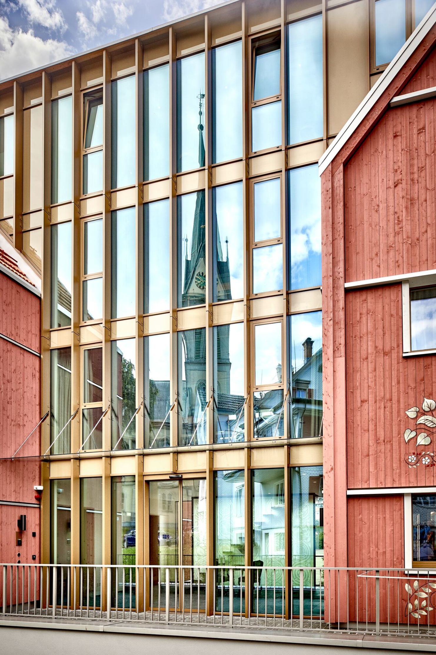 Façade moderne avec beaucoup de verre, dans laquelle se reflète le clocher de l'église