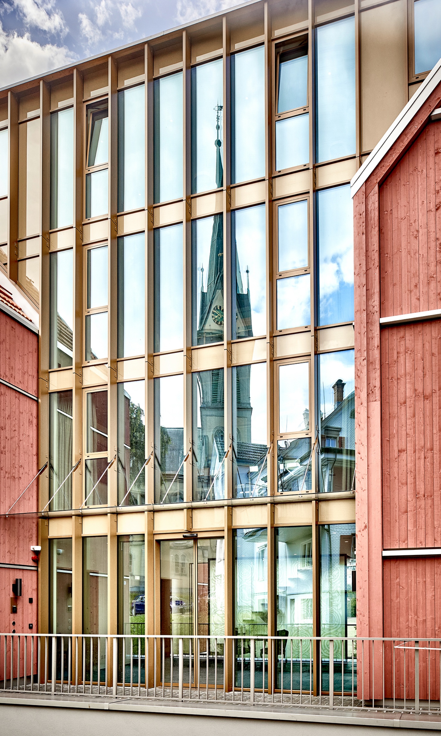 Moderne Fassade mit viel Glas, in der sich der Kirchturm spiegelt
