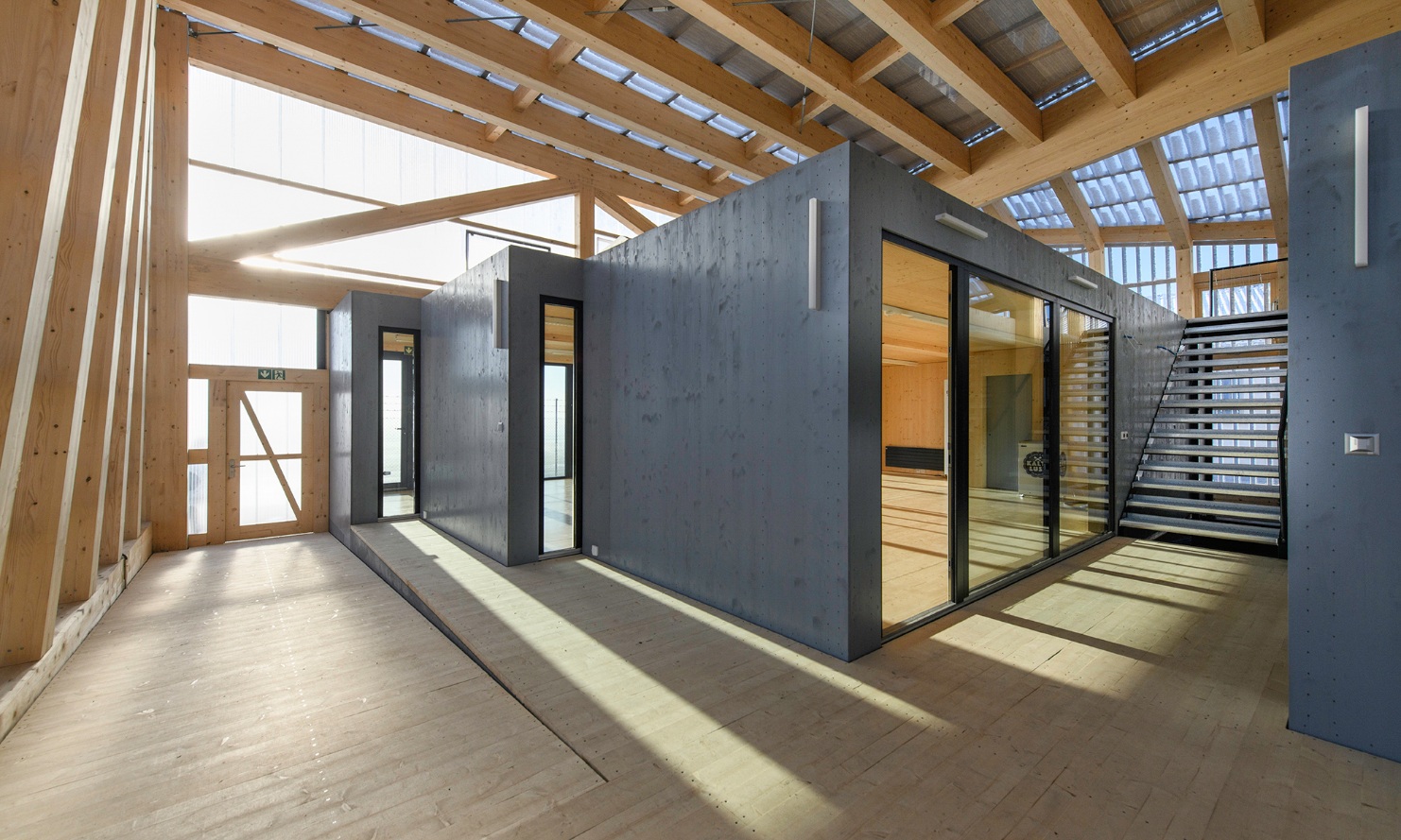 Des modules en bois de la taille d’une pièce définissent des unités spatiales à l’intérieur d’une halle en bois.