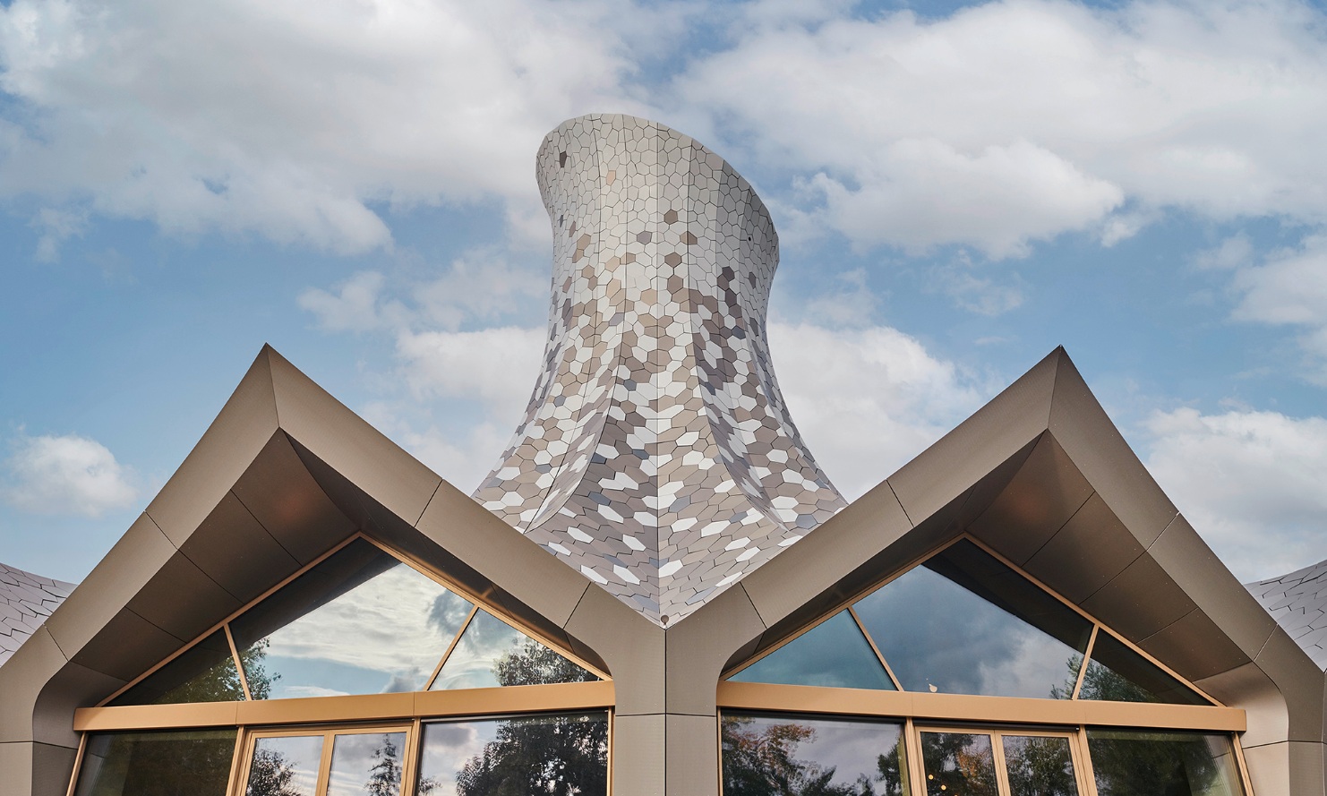 The cantilever timber roof, designed as a prismatic shell structure, is surrounded by irregularly shaped sheet metal sheds. 