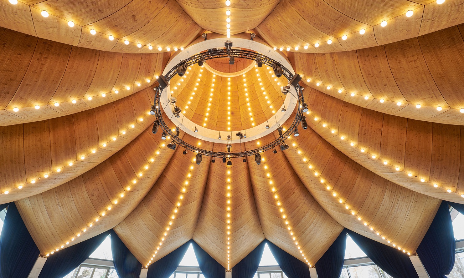 Dessous du toit incurvé en bois à formes libres, avec une guirlande lumineuse à l’intérieur du chapeau de magicien