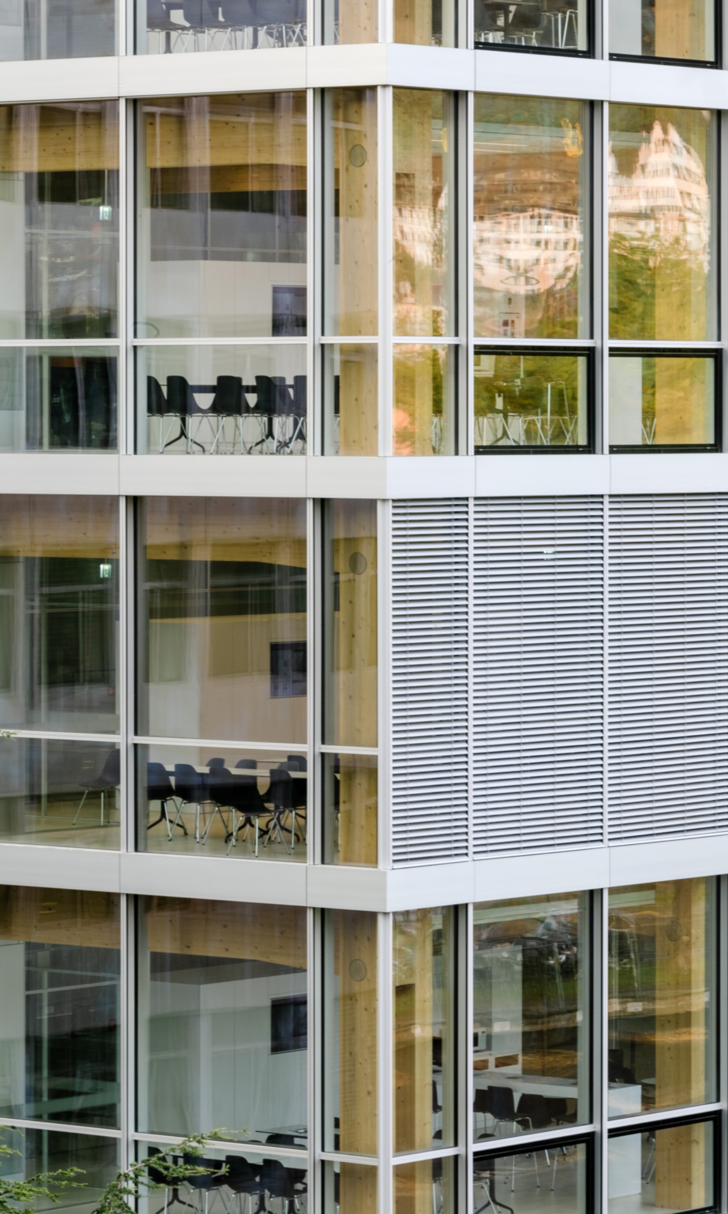 Vue extérieure de l’immeuble de bureaux Omega. A travers les fenêtres, on aperçoit les équipements de bureau et les poutres en bois massif