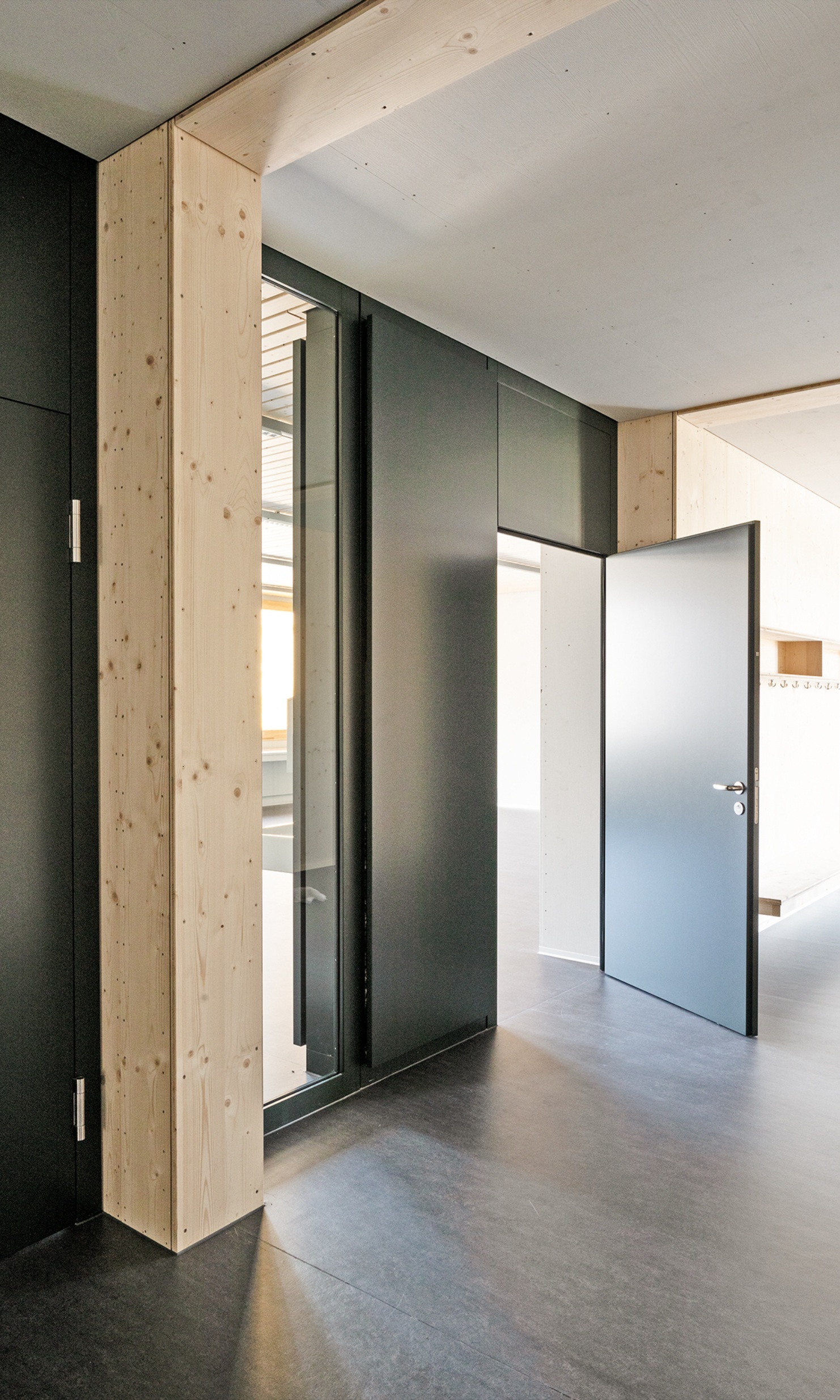 Entrée du pavillon scolaire de Brünnen avec des éléments en bois dans les tons noir et naturels