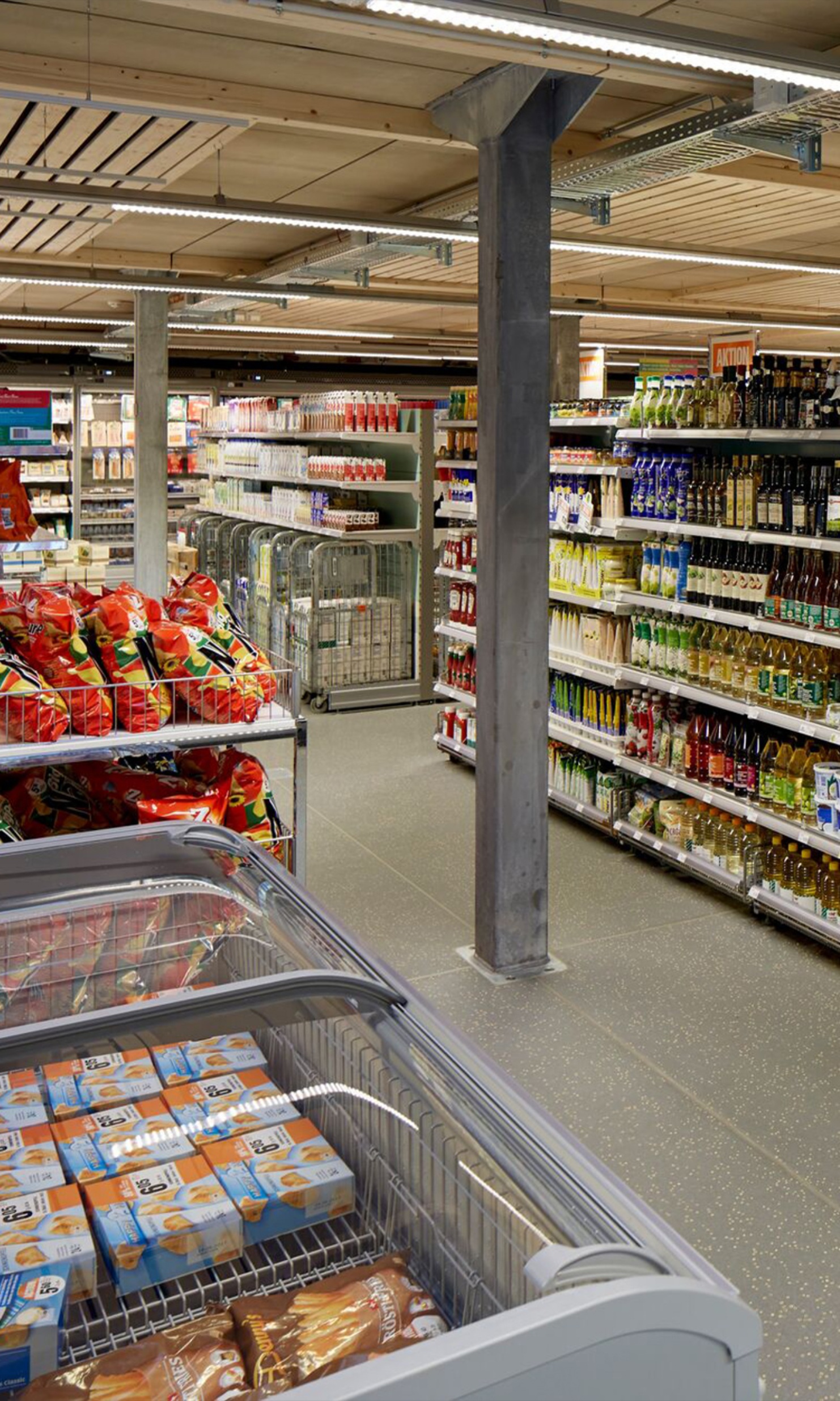 Innenansicht des Migros-Verkaufsprovisoriums; Gang mit Verkaufsgestellen auf beiden Seiten.