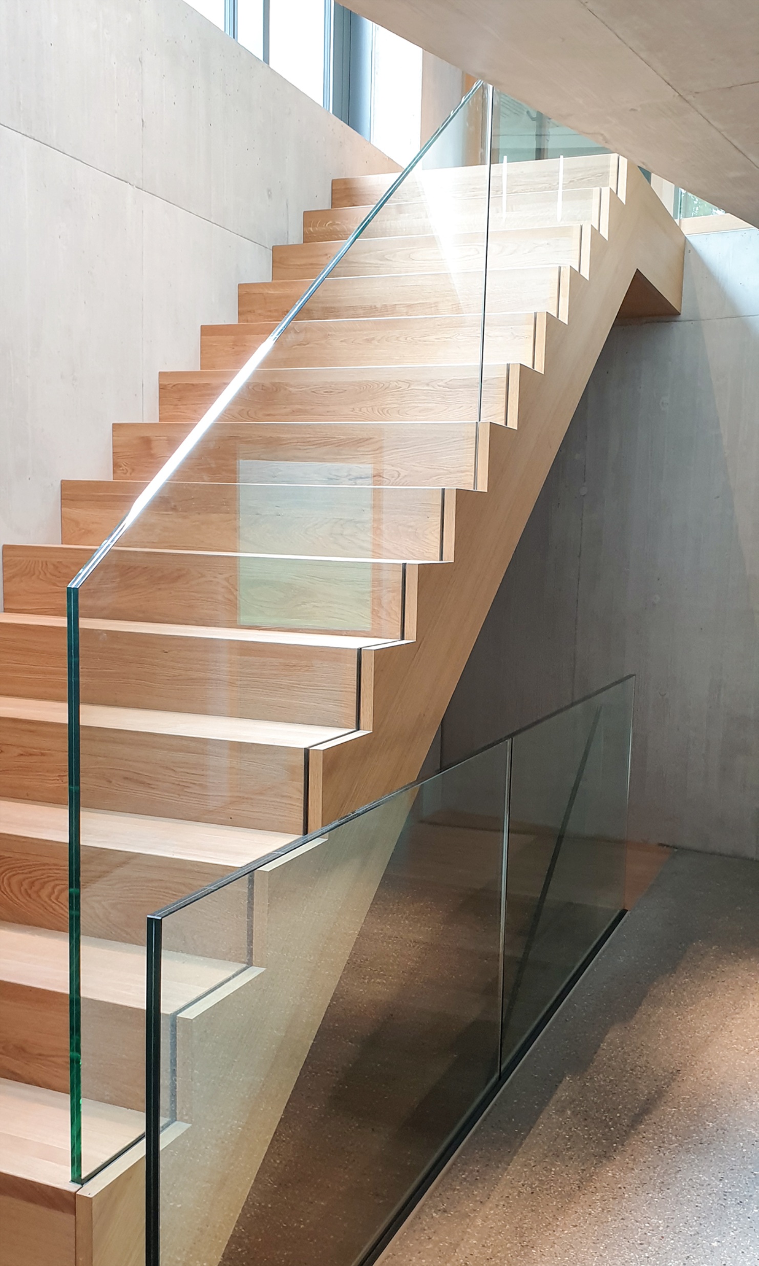 Un escalier sobre avec des marches en bois et une balustrade en verre relie le sous-sol au rez-de-chaussée.<br/><br/><br/><br/>
