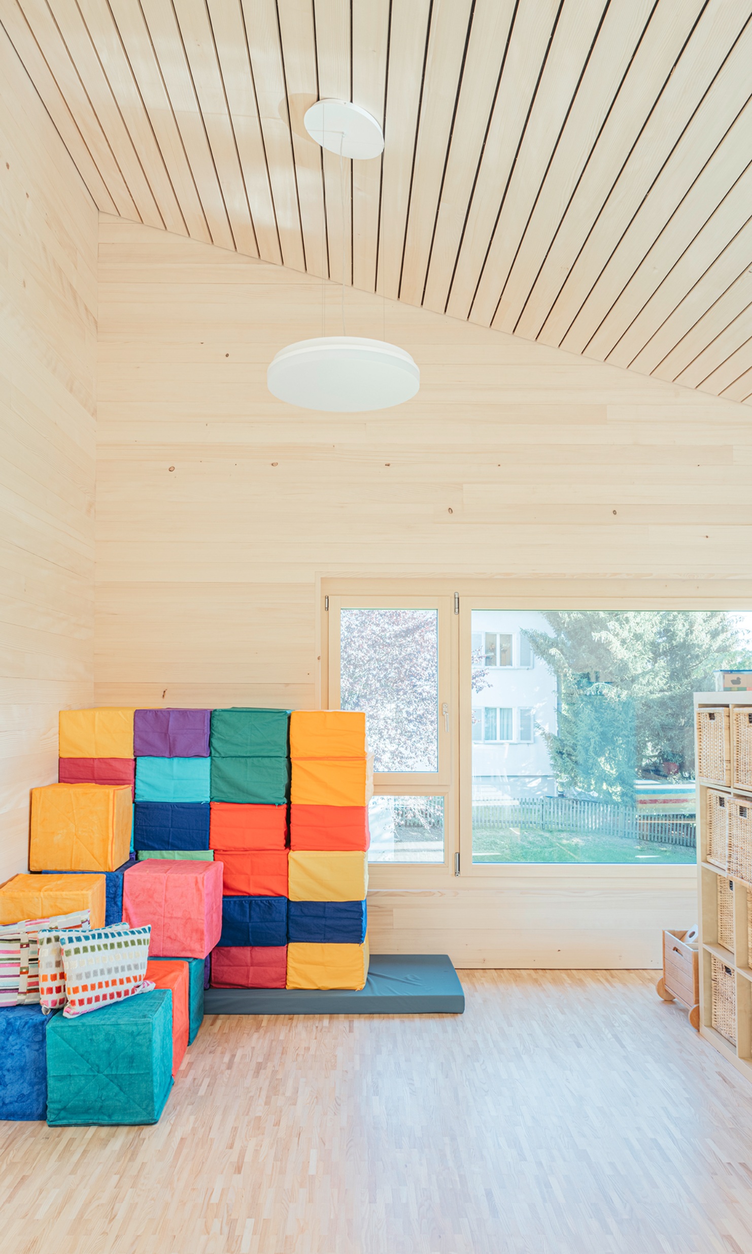 Spielzimmer mit abgeschrägter Holzdecke und aufgestapelten farbigen Sitzwürfeln