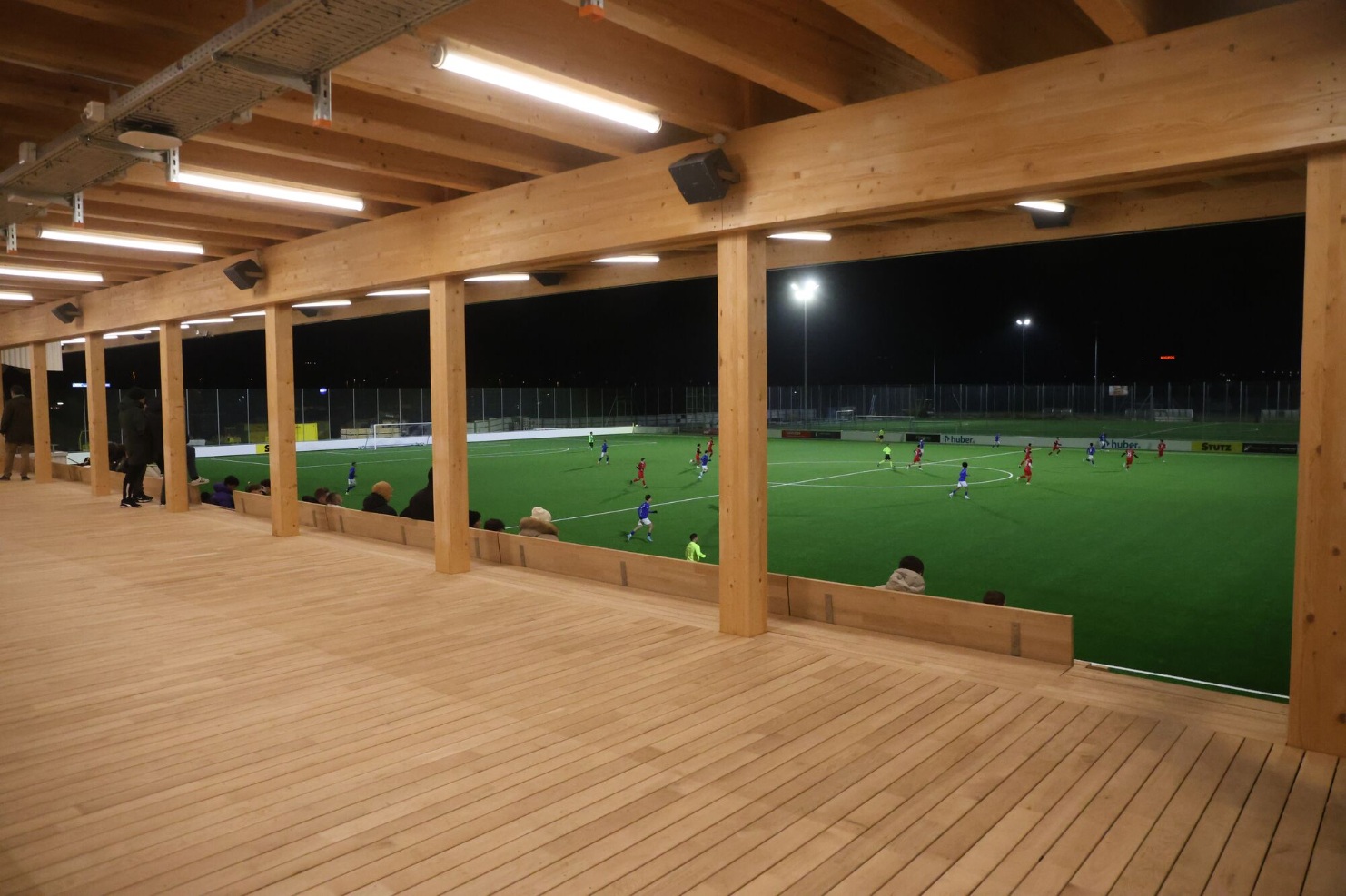Grosszügige Holzterrasse mit Blick auf das Spielfeld Holzterrasse mit Blick durch die offene Holzkonstruktion auf ein Fussballspiel in Gossau 