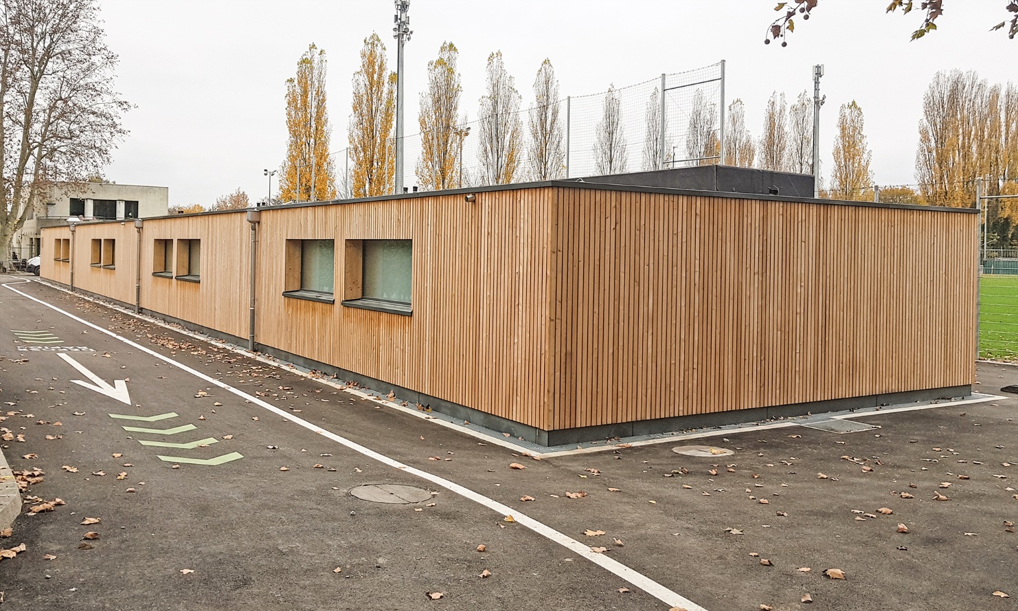 Eingeschossiger Erweiterungsbau mit Holzfassade für die Umkleideräume des Stade des trois Chênes