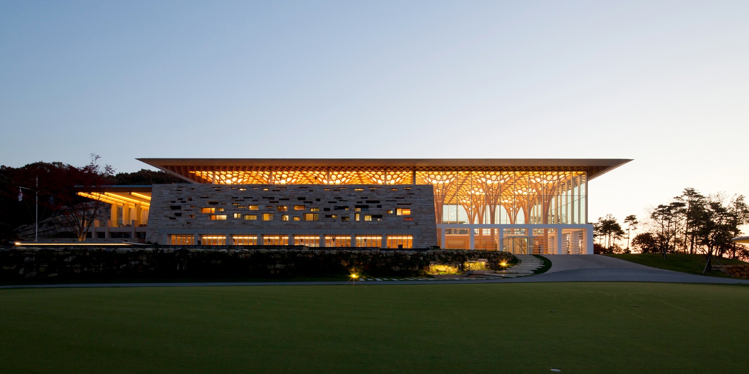 View of the illuminated clubhouse at dusk. The large windows provide views of the illuminated tree-like supporting structures.