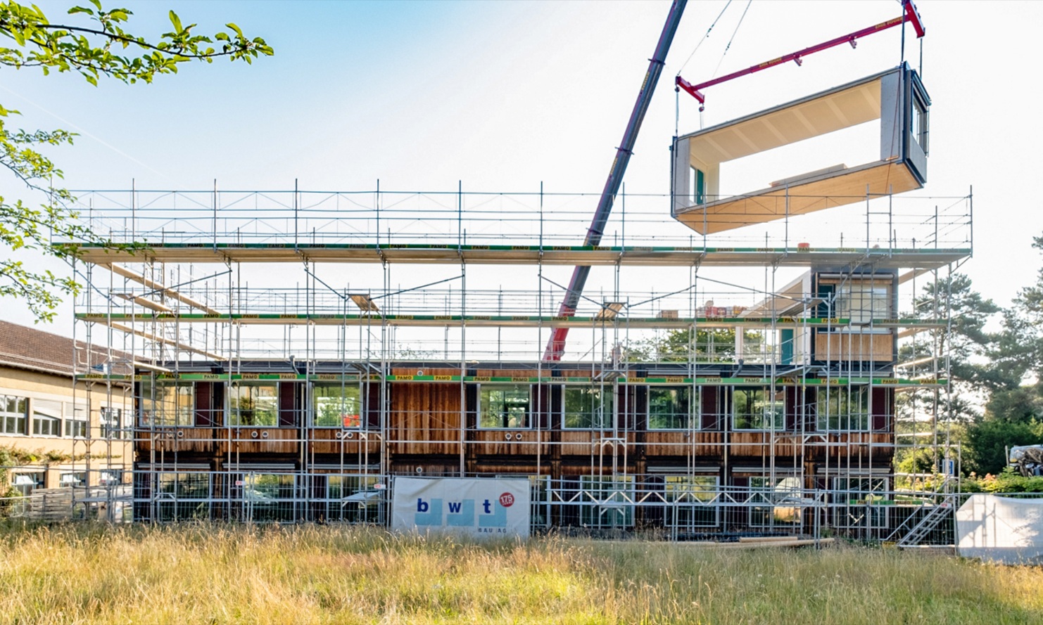 Das bestehende ZM10-Modulbau-Schulhaus Friesenberg wird um ein weiteres Stockwerk erweitert. Ein Holzmodul wird mit dem Kran auf dem Dach platziert. 