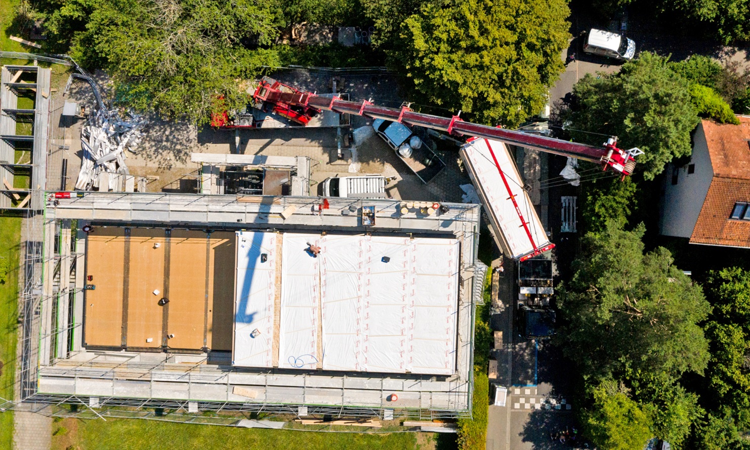 Luftaufnahme – von oben sind die fünf bereits platzierten Holzmodule zu sehen, die per Kran auf das Dach des Schulhauses gehievt wurden.