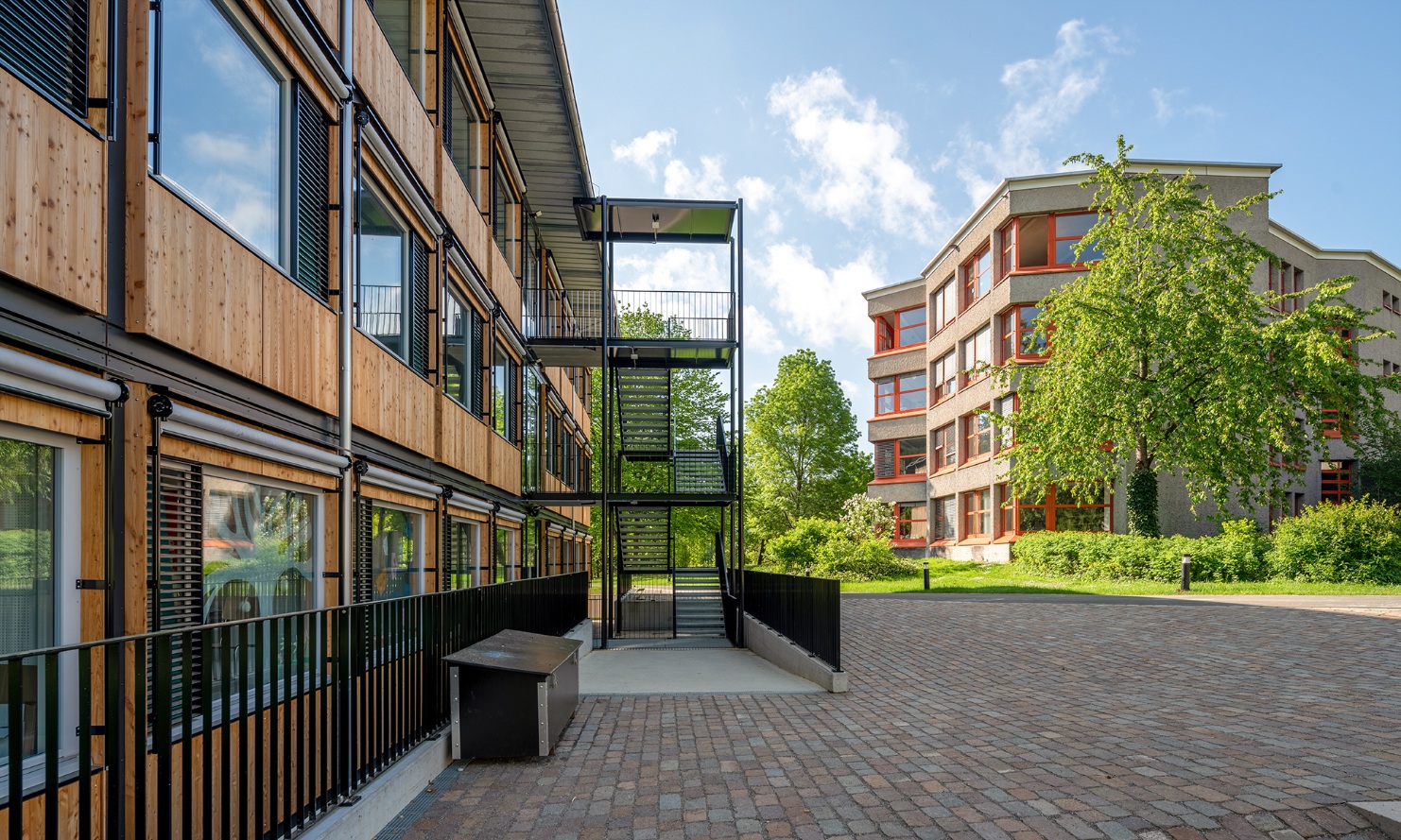 Externer Treppenaufgang und Fassade des ZM10-Schulpavillons Sihlweid in Zürich mit Schulhaus im Hintergrund