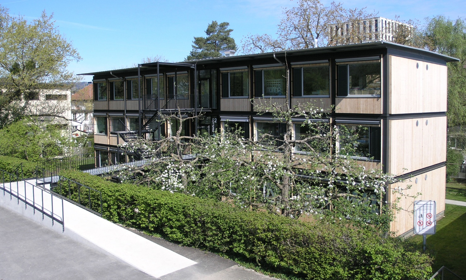 The photograph shows the entrance area to one of the modules for the City of Zurich. The module is somewhat hidden behind the greenery.