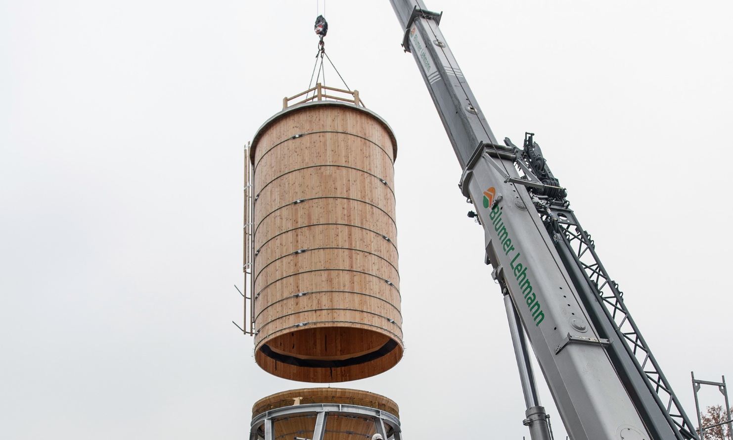 Round timber silo body dangling from a crane