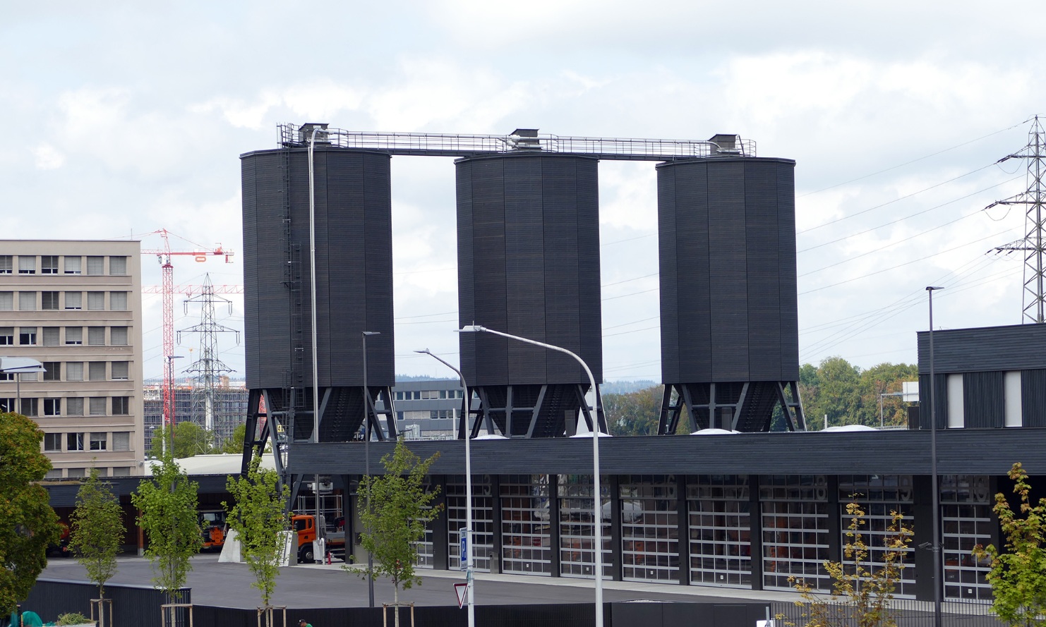 Trois silos dodécagonaux (E12) en bois, reliés avec support en acier et plateforme de toit en bois, placés derrière le parc de camions