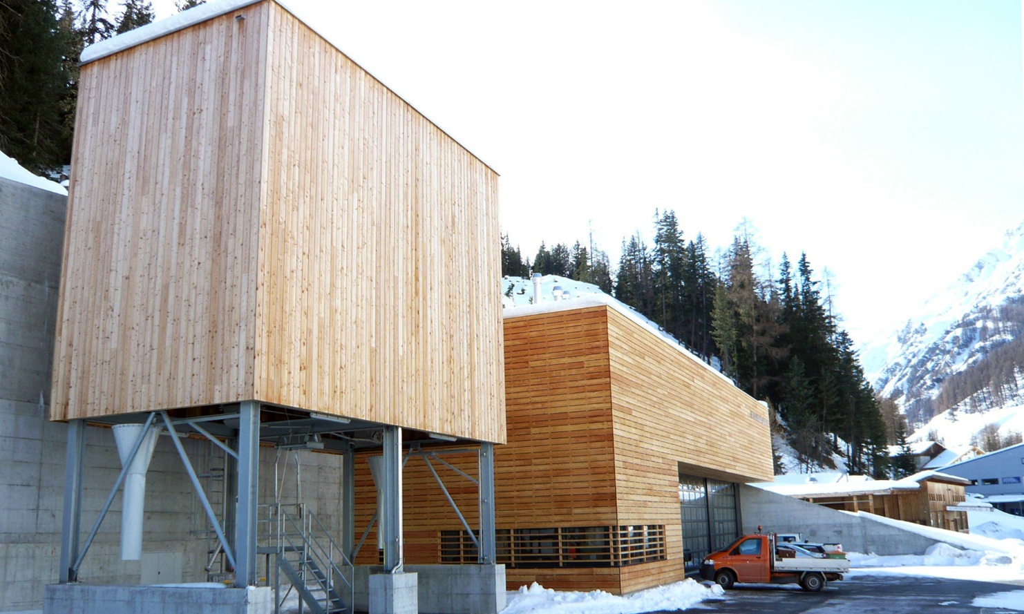 100 m³ timber modular silo with steel substructure, alongside a maintenance depot building with identical facade