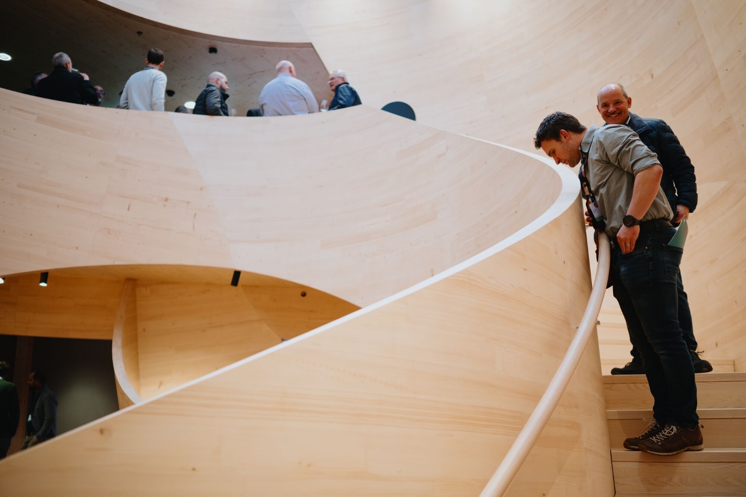 Besucher bestaunen die geschwungene Holztreppe im Atrium des Stammhauses von Blumer Lehmann beim 150-jaehrigen Jubilaeum.