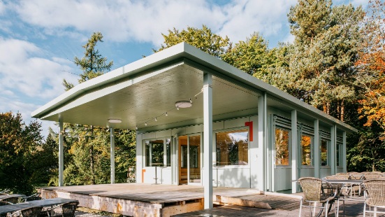 Sportfeld-Pavillon mit Terrasse und Sitzmöbeln.