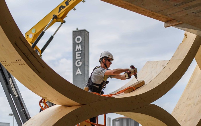 Der Montagemitarbeitende bohrt ein Loch in die Holzkonstruktion des Swatch-Gebäudes