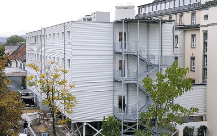 Gesamtansicht des dreigeschossigen Spitalprovisoriums St. Clara in Holzmodulbauweise mit Treppenzugang auf der Stirnseite des Gebäudes. 