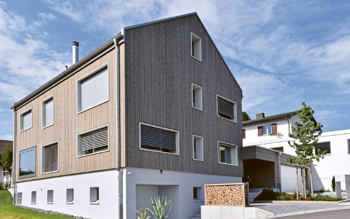 Gesamtaufnahme vom lichtdurchfluteten Einfamilienhaus mit Garten und einer Raumgestalt gefüllt mit Holzscheiter auf dem Kiesvorplatz