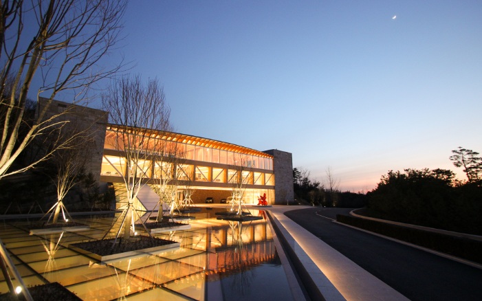 Vue extérieure du Haesley Nine Bridges Golf Resort Learning Centre. Architecture en bois éclairée la nuit avec un étang au premier plan.