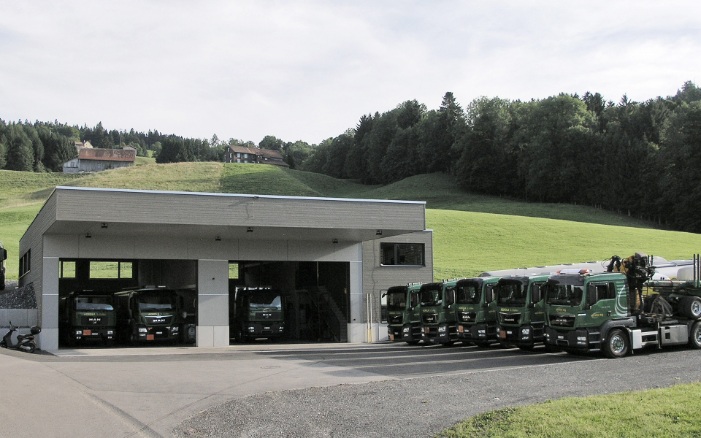 Gesamtansicht der Lkw-Einstellhalle mit parkierter Lkw-Flotte davor. 