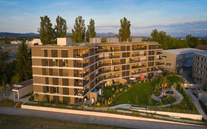 Vue panoramique du projet Sunnehof, qui compte six étages, depuis le côté. La forme incurvée du bâtiment et les nombreux éléments en bois sont frappants.