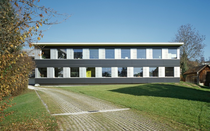 Zweigeschossiger temporärer Schulpavillon Hasenacker in Männedorf steht auf grüner Wiese.