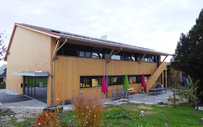 Gesamtaufnahme von Bio-Bäckerei mit Garten sowie Aussenbestuhlung und farbenfrohen Sonnenschirmen