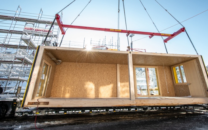 Holzmodul am Kran: LKW-Ablad auf der Baustelle bei strahlender Wintersonne.