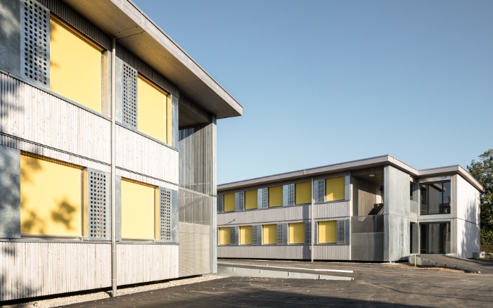 Zweigeschossige Schulpavillons Brünnen mit Holzfassaden und gelben Rollläden
